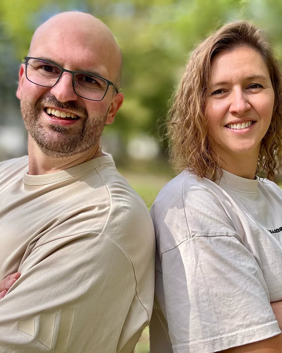 Dominik Frank und Stefanie Klaue, das Gründerteam von CheckerHero, Rücken an Rücken lächelnd in einem sonnigen Park