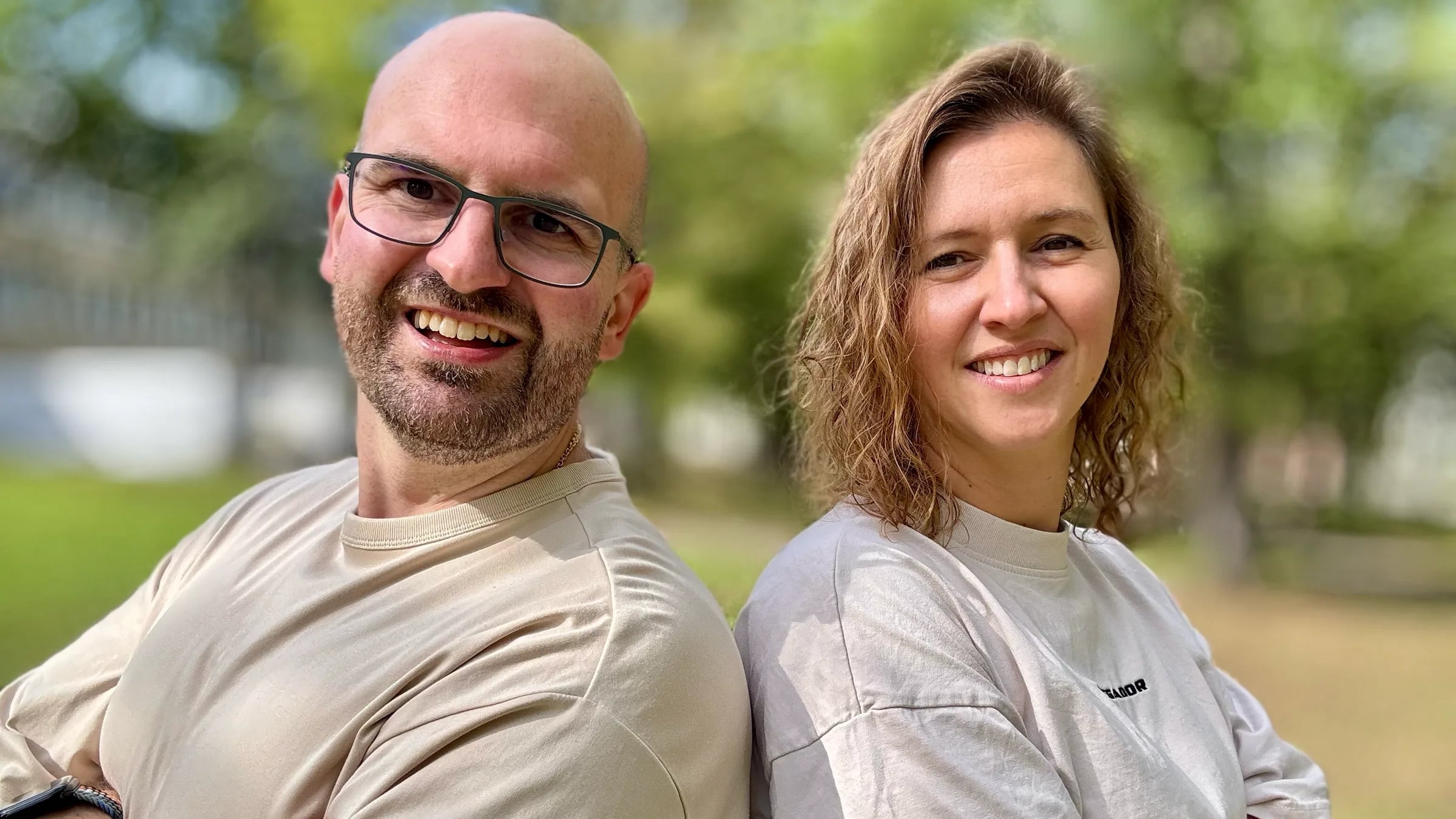 Dominik Frank und Stefanie Klaue, das Gründerteam von CheckerHero, Rücken an Rücken lächelnd in einem sonnigen Park
